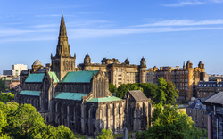 Glasgow Kathedrale in Schottland, umgeben von Stadtgebäuden und grünen Bäumen, bei klarem Himmel.