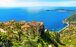 Mittelmeer-Küstenlandschaft mit Dorf auf Hügel und weitem Meerblick.