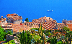 Blick über mediterranes Dorf mit Kakteen und Meer im Hintergrund.