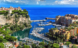Hafen von Monaco mit Yachten und Gebäuden vor blauem Meer und Himmel.