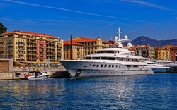 Luxusyacht im Hafen vor einer Stadtkulisse mit Bergen im Hintergrund.