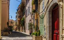 Enge, sonnige Gasse mit bunten Häusern und Pflanzen in Töpfen an den Türen.