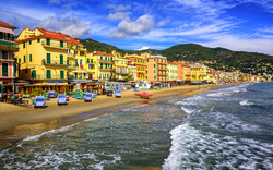 Strandpromenade mit bunten Gebäuden am Meer, sanfte Wellen und blauer Himmel.
