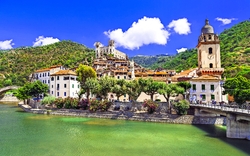 Mittelalterliche Stadt mit Fluss und Hügeln im Hintergrund bei sonnigem Wetter.