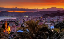 Stadtansicht bei Sonnenuntergang mit Kirchengebäude und Palmen im Vordergrund.