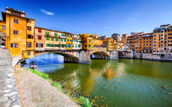 Brücke Ponte Vecchio in Florenz über Fluss Arno mit bunten Gebäuden im Hintergrund.
