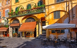 Bunte Fassade eines Restaurants mit Außensitzbereich auf einem sonnigen Platz.