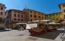 Marktplatz in Pistoia, Toskana, Italien mit bunten Gebäuden und Marktständen bei sonnigem Wetter.