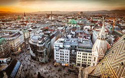 Luftaufnahme von Wien bei Sonnenuntergang, zeigt die Stadtlandschaft mit Gebäuden und Straßen.