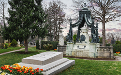 Ein Grabmal auf dem Wiener Zentralfriedhof, umgeben von Bäumen und Blumenbeeten im Frühling.