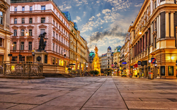 Prachtstraße mit historischen Gebäuden und einer Barocksäule bei Sonnenuntergang in der Stadt.