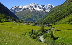 Alpentäler im Sommer mit Bergbach und schneebedeckten Gipfeln im Hintergrund.