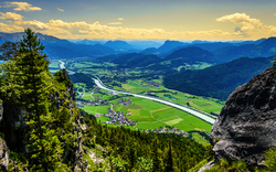 Landschaftspanorama mit Fluss, Bergen und grünem Tal im Sonnenschein.