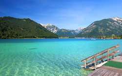 Steg am türkisfarbenen Bergsee mit Bergen im Hintergrund unter blauem Himmel.