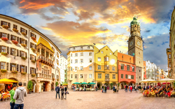 Historischer Platz mit bunten Gebäuden und Turm bei Sonnenuntergang.