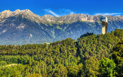 Wald und Bergkette mit Skisprungschanze unter blauem Himmel