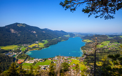 Blick auf einen klaren blauen See inmitten grüner Berge und Dörfer.