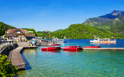 See mit Booten und Steg vor Bergkulisse bei klarem Himmel.