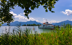 Boot auf einem See, umgeben von Bergen und Schilf, unter einem blauen Himmel