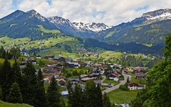 Dorf in den Alpen mit Häusern, Wiesen und schneebedeckten Bergen im Hintergrund