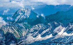 Berglandschaft mit schneebedeckten Gipfeln und Wolken am Himmel.
