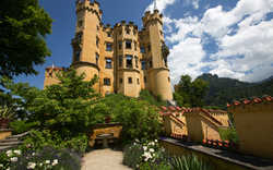 Gelbes Schloss mit Türmen und Garten im Vordergrund, sonniger Tag.