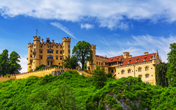 Schloss Hohenschwangau in Bayern, umgeben von grüner Landschaft und blauem Himmel.