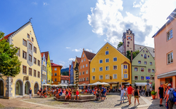 Bunter Platz mit Menschen und historischen Gebäuden bei Sonnenschein.