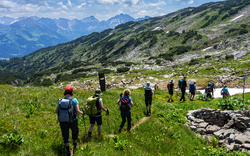Gruppe von Wanderern auf einem Bergpfad in alpiner Landschaft.
