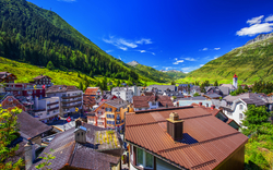 Bergdorf in den Alpen mit bunten Häusern und bewaldeten Hügeln im Hintergrund.