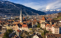 Panorama einer Stadt mit Kirche und Bergen im Hintergrund.