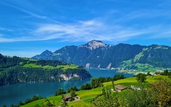 Landschaft mit See, Bergen und grünem Tal unter blauem Himmel.