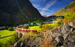 Roter Zug auf einem Viadukt in alpiner Landschaft bei sonnigem Wetter.