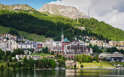 Kleinstadt am See vor bewaldeten Hügeln und Bergen im Hintergrund