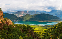 Blick auf einen See und umliegende Berge durch eine bewaldete Schlucht.