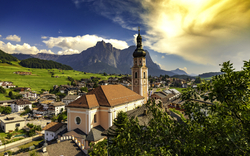 Kleine Stadt mit Kirche vor Bergkulisse bei Sonnenuntergang.