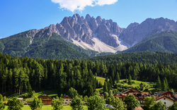 Alpenlandschaft mit Bergen, Wald und Dorf im Tal bei klarem Himmel.