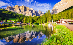 Alpenlandschaft mit See, Bergen und Wald im Sonnenschein.