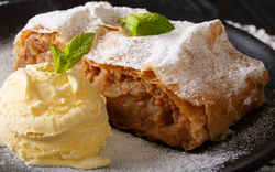 Apfelstrudel mit Vanilleeis und Minzblättern auf schwarzem Teller.