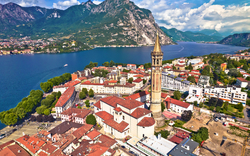 Luftaufnahme einer Stadt am See mit Gebirge im Hintergrund.