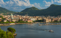 Stadtansicht am See mit Bergen im Hintergrund bei klarem Himmel.