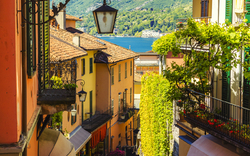 Blick auf enge Gasse mit bunten Häusern und Seepanorama in bergiger Landschaft.