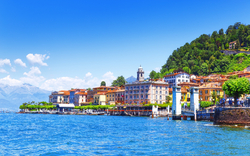 Uferpromenade einer Stadt am See mit Bergen im Hintergrund bei klarem Wetter.