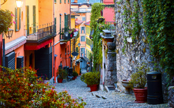 Gepflasterte Straße durch Bellagio am Comer See mit bunten Gebäuden und Pflanzen an den Fassaden.