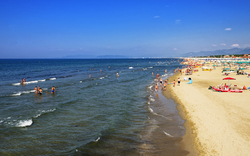 Strand mit Badegästen und Sonnenschirmen entlang der Küste bei klarem Himmel.