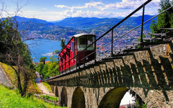 Rote Standseilbahn auf Schienen mit Blick auf einen See und Berge im Hintergrund.
