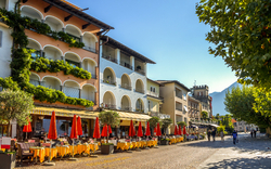Belebte Straße mit Restaurantterrassen und Sonnenschirmen.