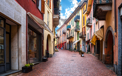 Enge gepflasterte Gasse mit bunten Häusern und Balkonen.