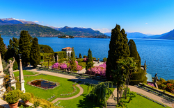 Blick auf gepflegten Garten mit See und Bergen im Hintergrund.