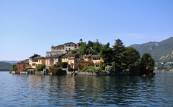 Insel mit bunten Häusern und Bäumen auf einem See vor Bergkulisse